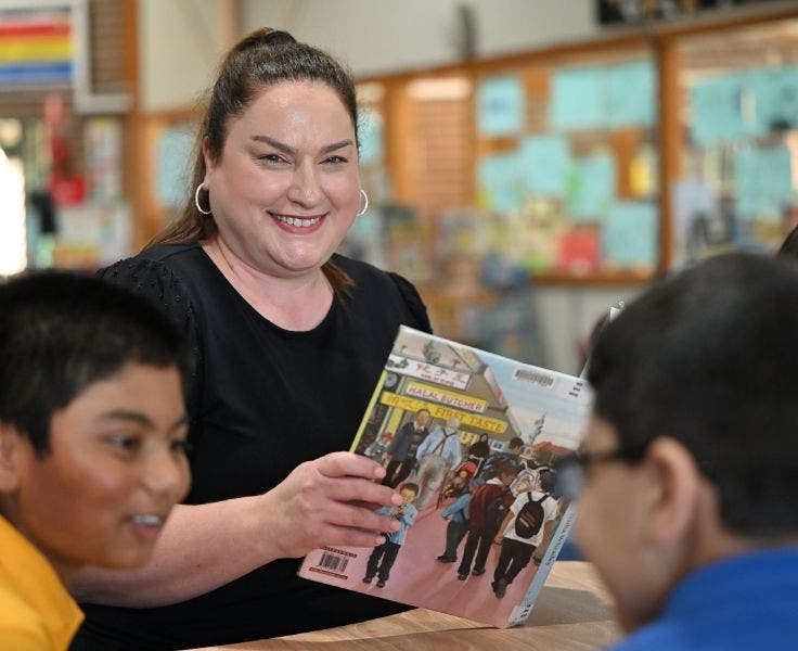 This is a photo of the school principal. She is holding a book and smiling at the camera. Two boys are in front of her and they are smiling.