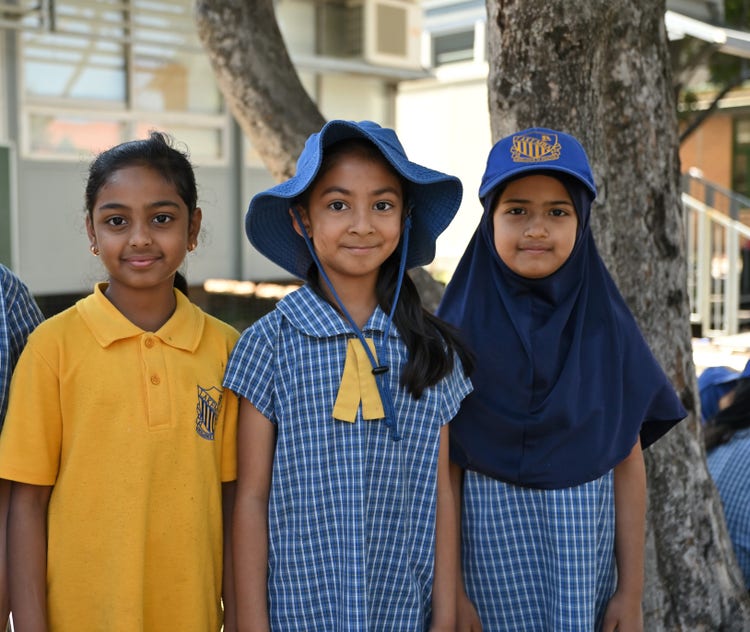 Three girls are proudly wearing the school uniform. They are standing in the playground.