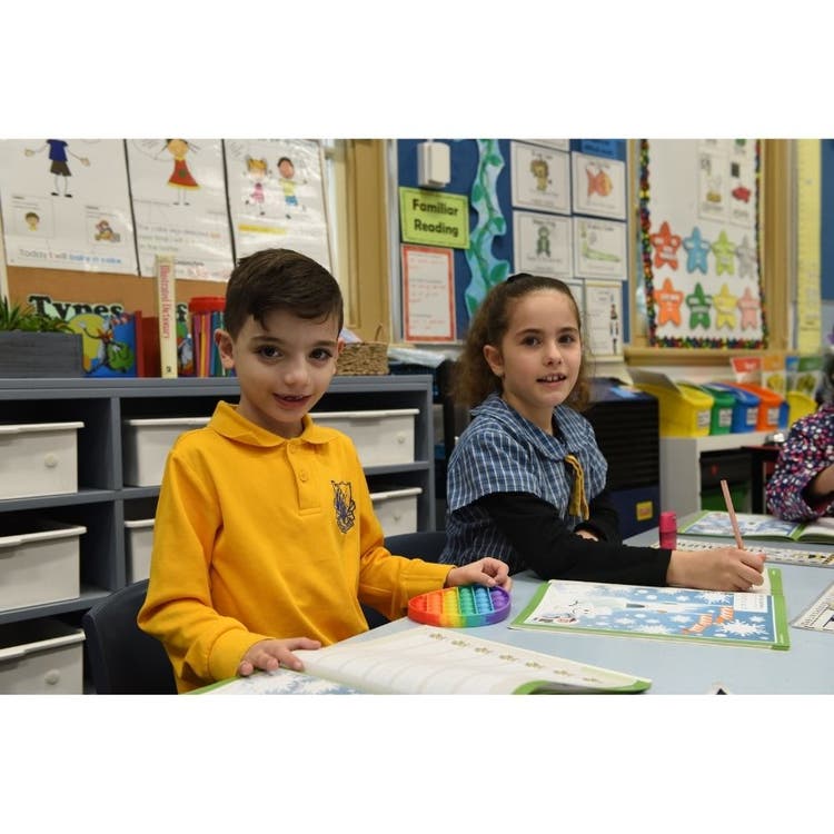 A young boy and girl sitting at their desks with school work in front of them.