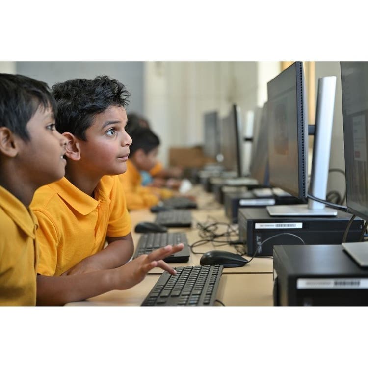 Two boys are sitting down at the computer. They are typing on the keyboard and looking at the screen.
