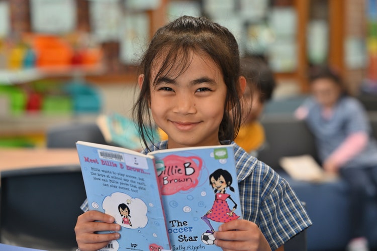 This shows a female student holding a book and smiling.