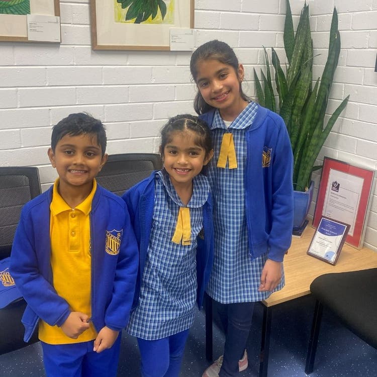 One boy and two girls are standing in the front office and are smiling. They are the winners of the 2025 public speaking competition.