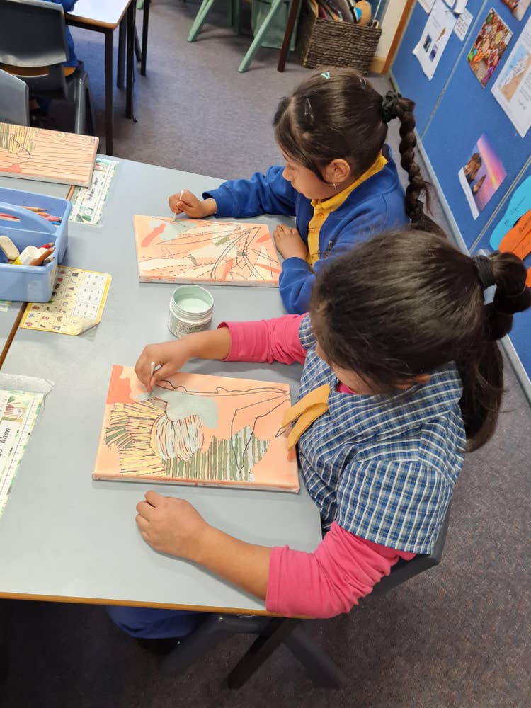 Two girls are sitting at their desks and creating an artwork each.
